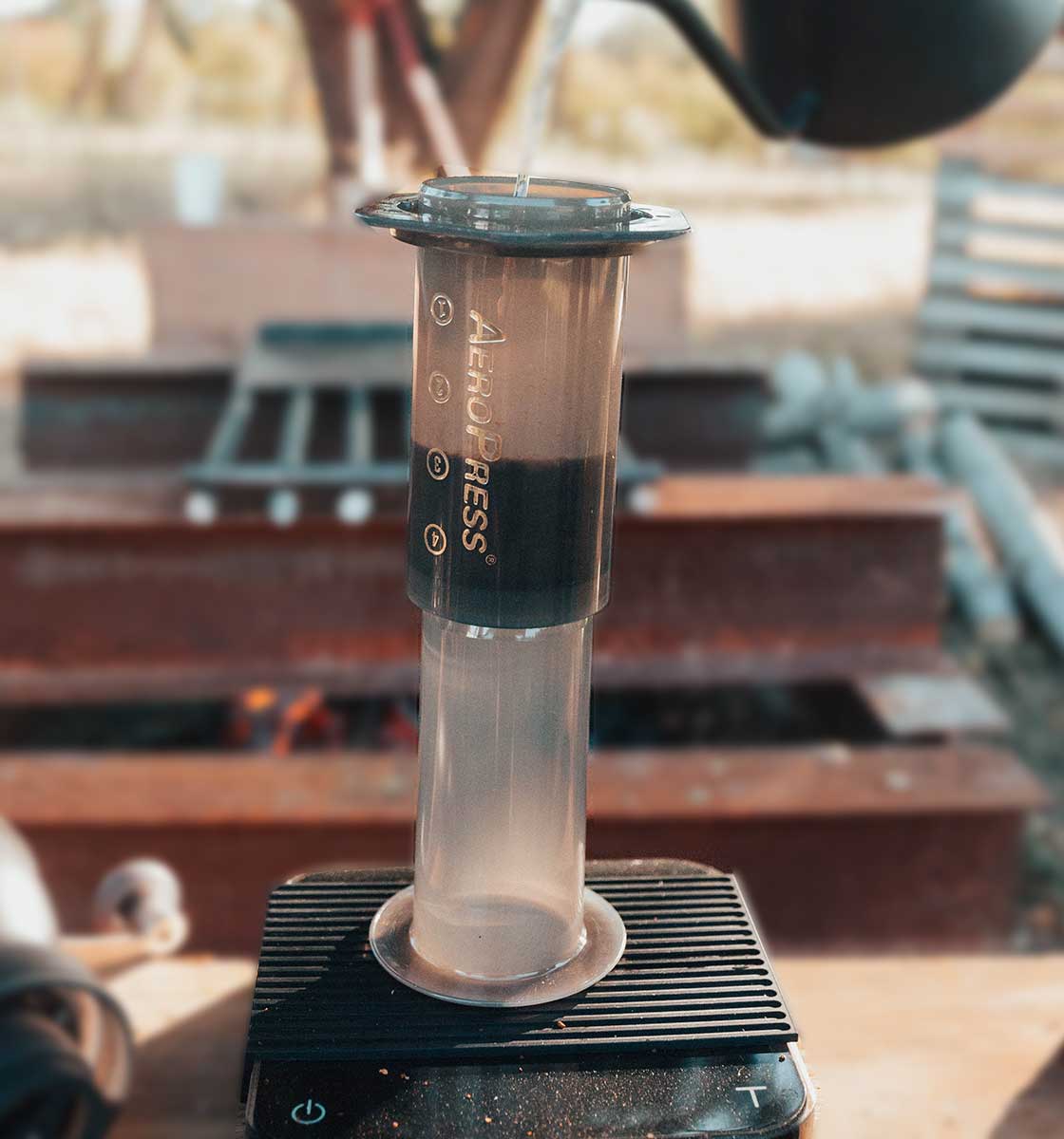 Açık havada hassas tartı üzerinde yer alan Aeropress filtre kahve demleme ekipmanına bariste kettle ile sıcak su doldurularak gerçekleştirilen fitre kahve demlemesi.