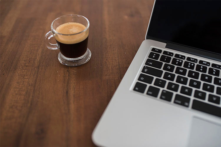 Kahverengi masa üstünde bir shot espresso ve macbook