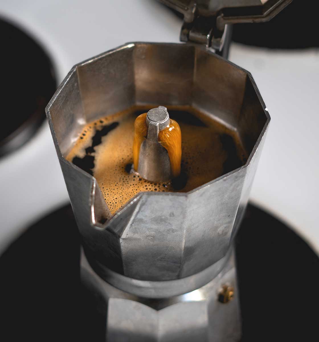 ocak üzerinde kahve demlenen kapağı açık bir moka pot'un üst açıdan çekilmiş görseli.